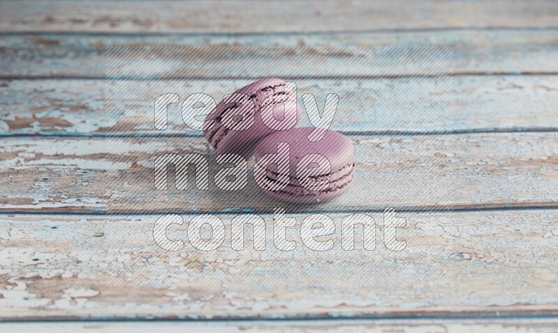 45º Shot of two Purple Blueberry macarons on light blue wooden background
