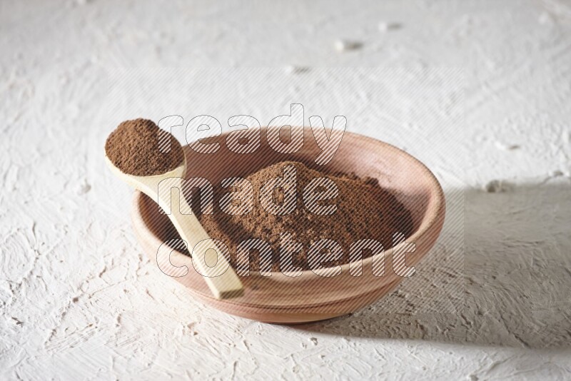 A wooden bowl and a wooden spoon full of cloves powder on a textured white flooring