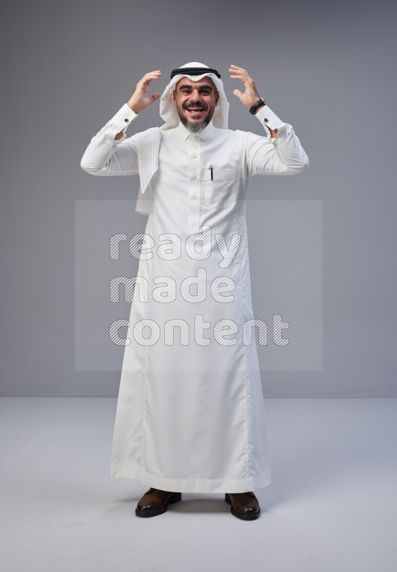Saudi man Wearing Thob and white Shomag standing interacting with the camera on Gray background