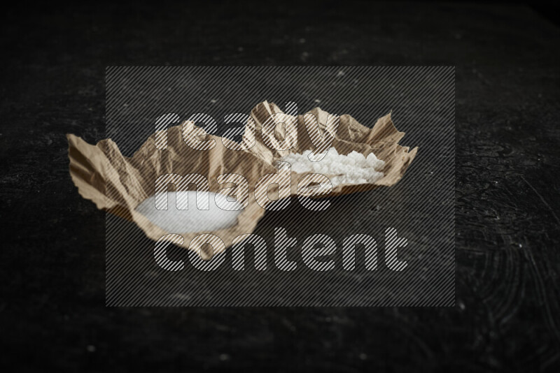A crumpled piece of paper full of white salt on black background