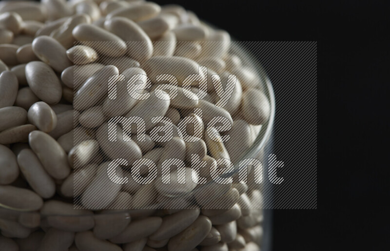 White beans in a glass jar on black background