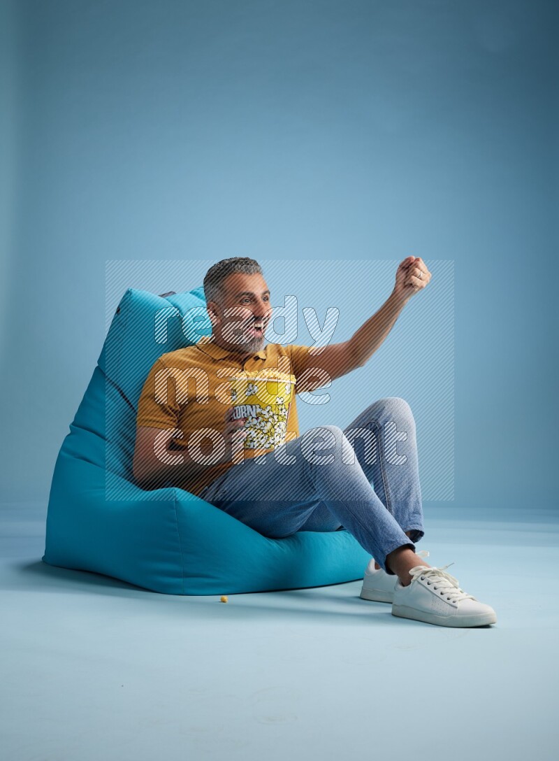 A man sitting on a blue beanbag and eating popcorn
