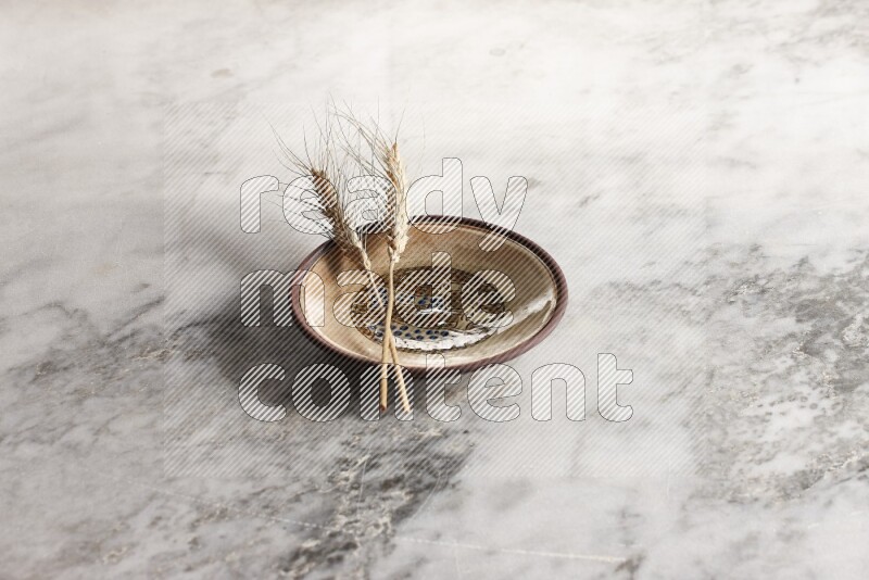 Wheat stalks on decorative pottery plate on grey marble background
