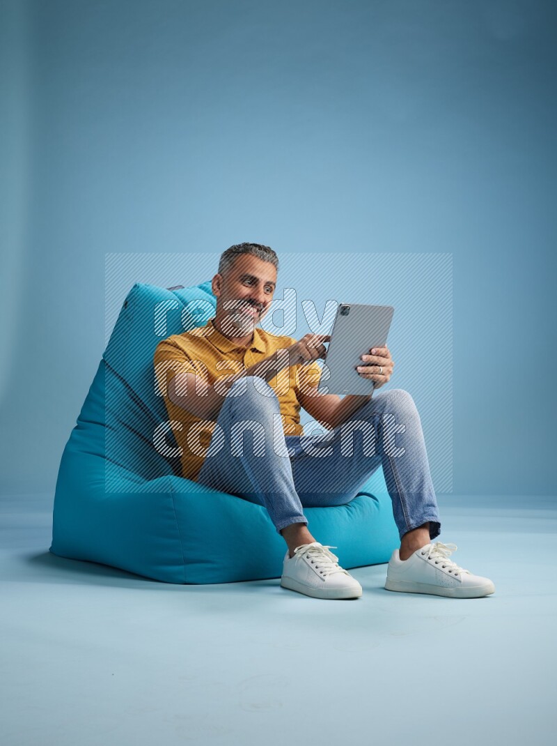 A man sitting on a blue beanbag and working on tablet