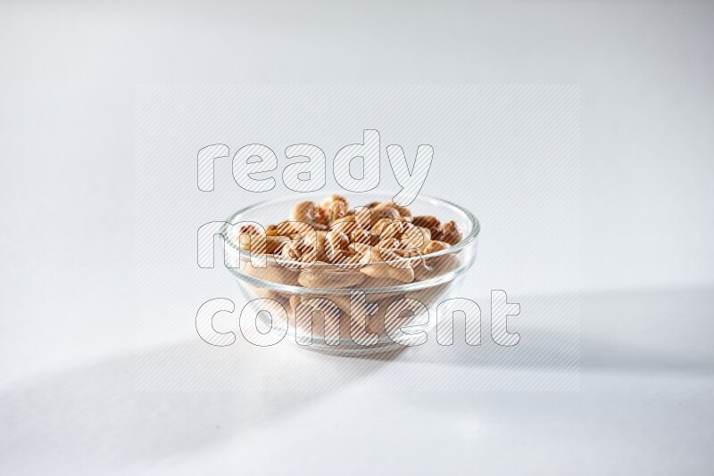 A glass bowl full of cashews on a white background in different angles