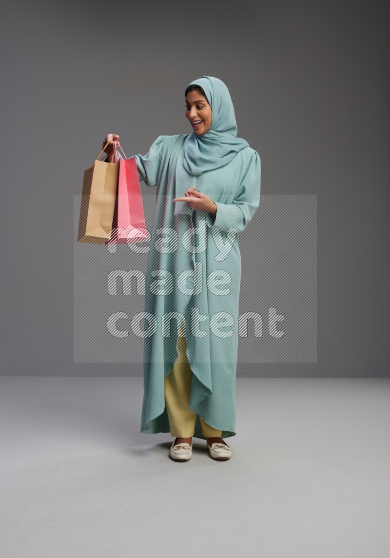 Saudi Woman wearing Abaya standing holding shopping bag on Gray background
