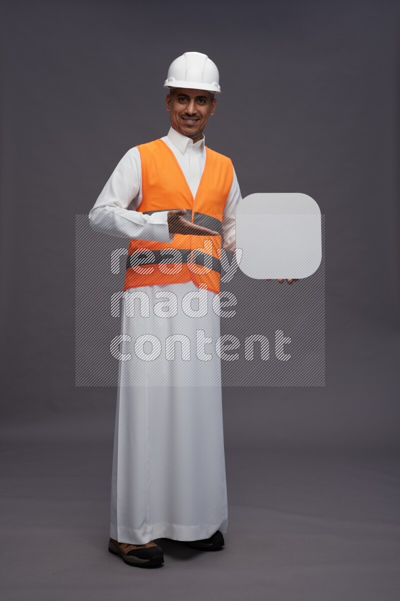 Saudi man wearing thob with engineer vest standing holding social media sign on gray background