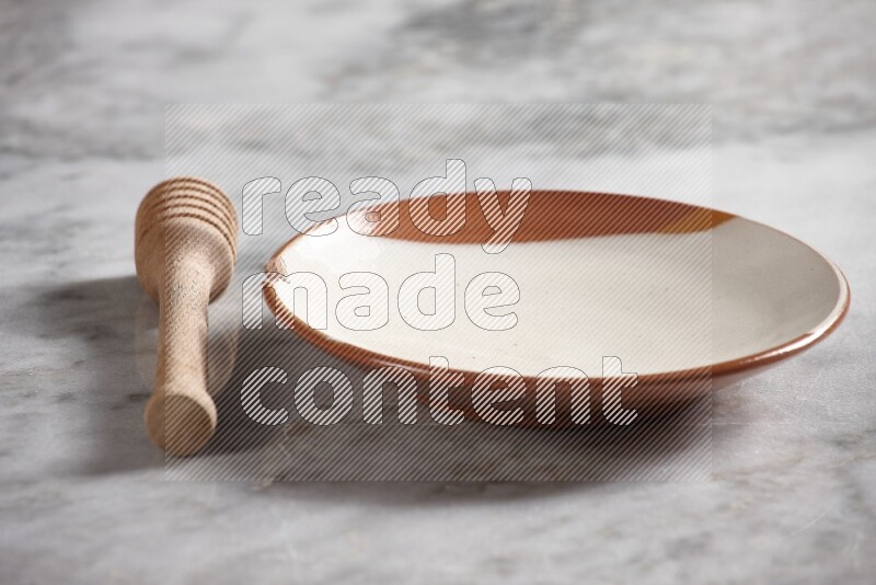 Multicolored pottery plate with wooden honey dipper on the side on grey marble background