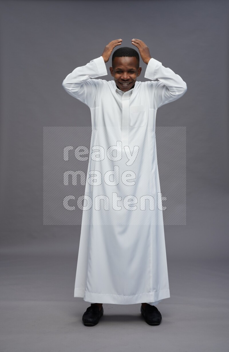 Saudi man wearing thob standing hands behind head on gray background