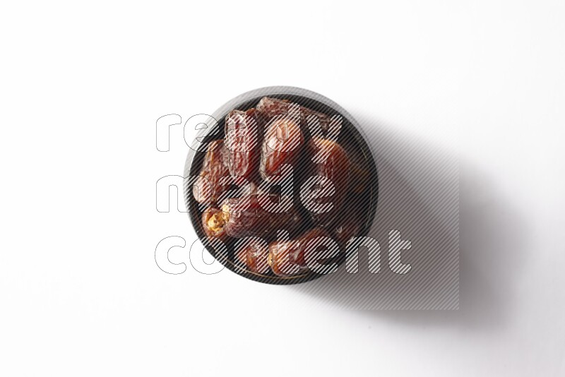 Dates in a black pottery bowl on white background