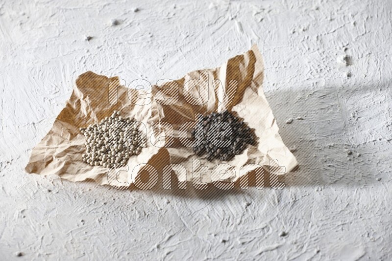 2 Crumpled pieces of paper full of black and white pepper beads on a textured white flooring