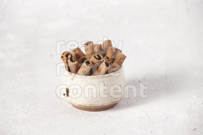 Cinnamon sticks in a beige bowl on a white background