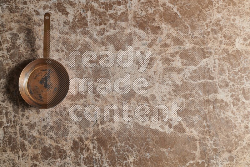 A small copper pan on beige marble background