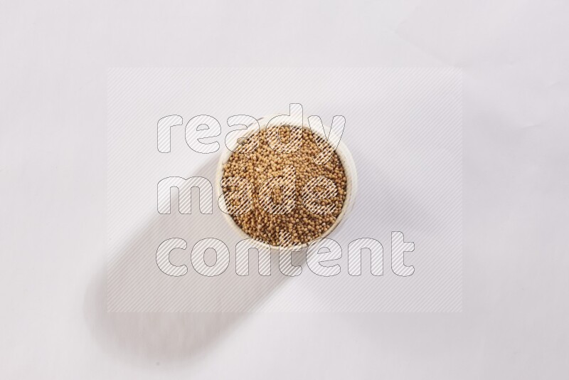 A beige pottery bowl full of mustard seeds on white flooring