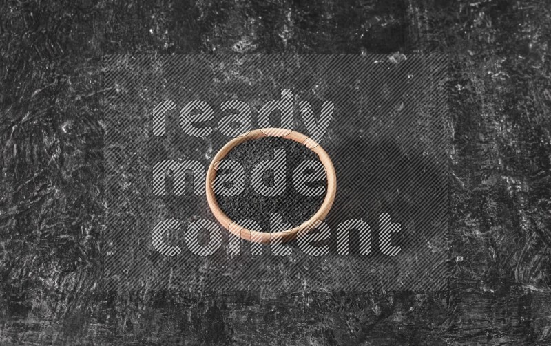 A wooden bowl full of black seeds on a textured black flooring