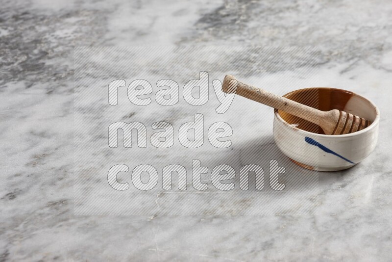 Multicolored pottery bowl with wooden honey dipper in it on grey marble background
