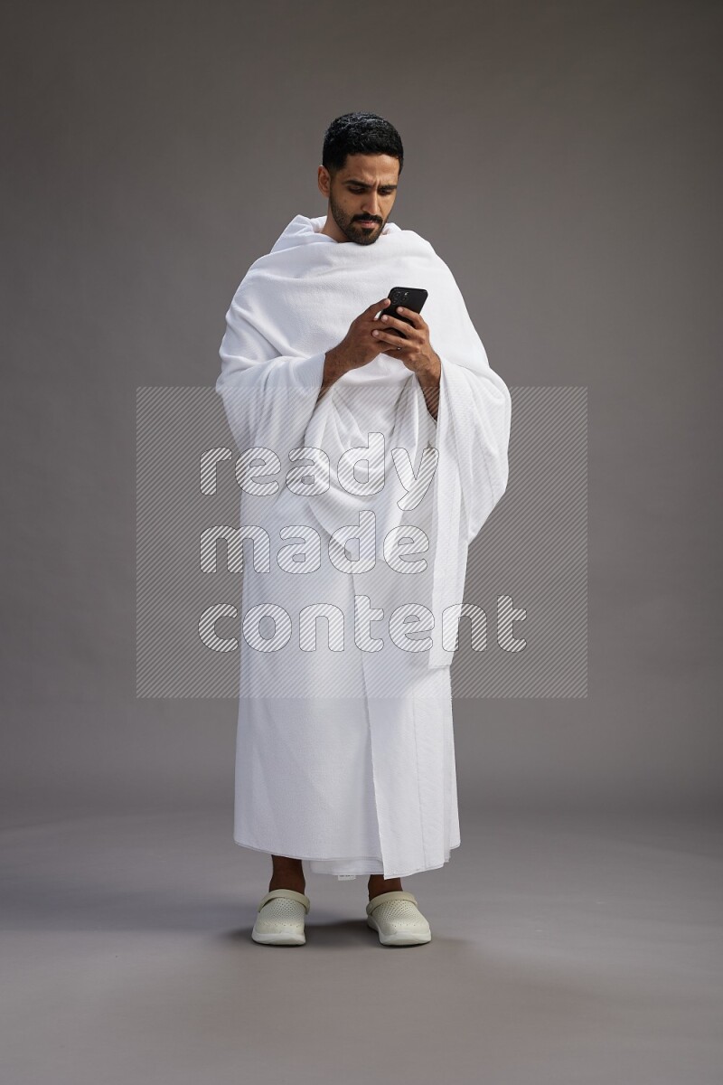 A man wearing Ehram Standing texting on phone on gray background