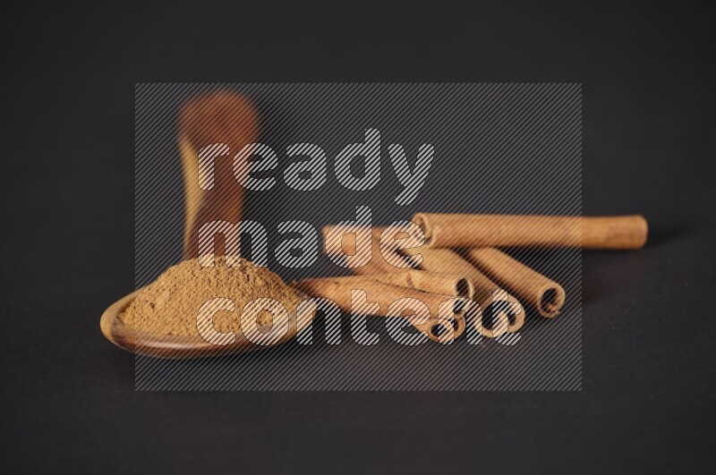 Cinnamon powder in a wooden ladle spoon beside it cinnamon sticks on the flooring on black background in different angles