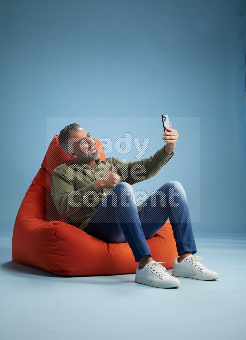 A man sitting on an orange beanbag and taking selfie