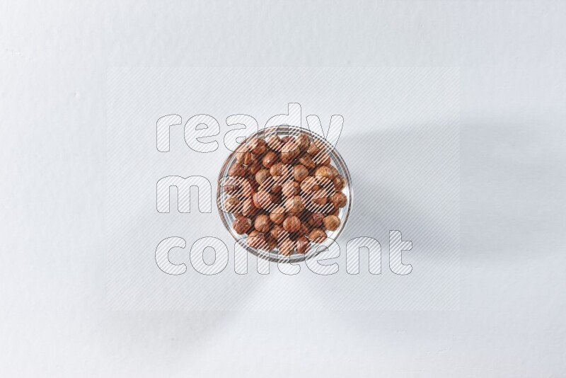 A glass bowl full of peeled hazelnuts on a white background in different angles