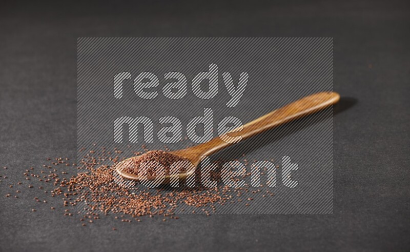 A wooden ladle full of garden cress seeds and seeds spread beside it on a black flooring