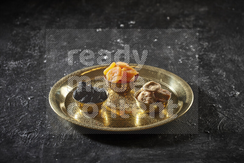 Dried fruits in metal bowls on a tray in a dark setup