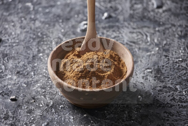 Wooden bowl full of cinnamon powder with a wooden spoon on a textured black background in different angles