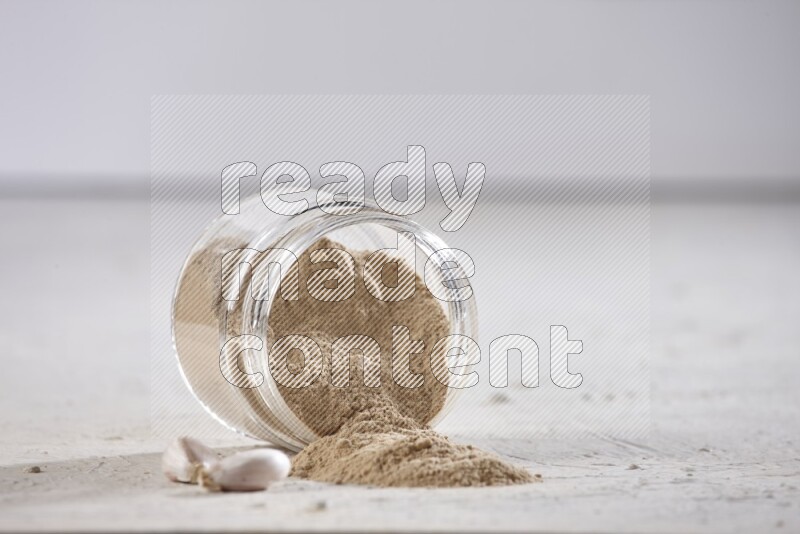 A glass jar full of garlic powder flipped over with the powder came out on a textured white flooring
