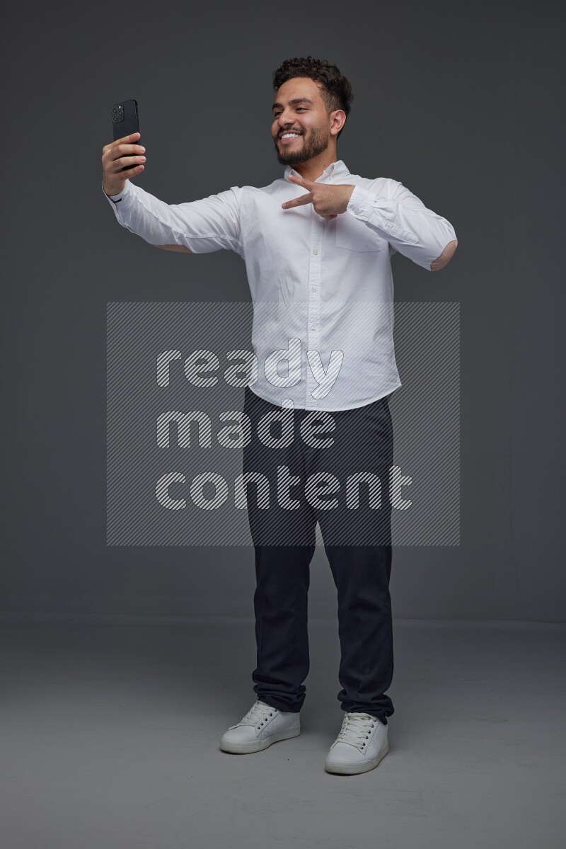 A man wearing smart casual and taking selfie with his phone eye level on a gray background