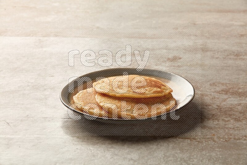 Three stacked plain pancakes in a bicolor plate on beige background