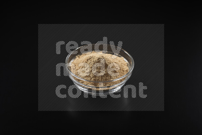 A glass bowl full of ground ginger powder on black background