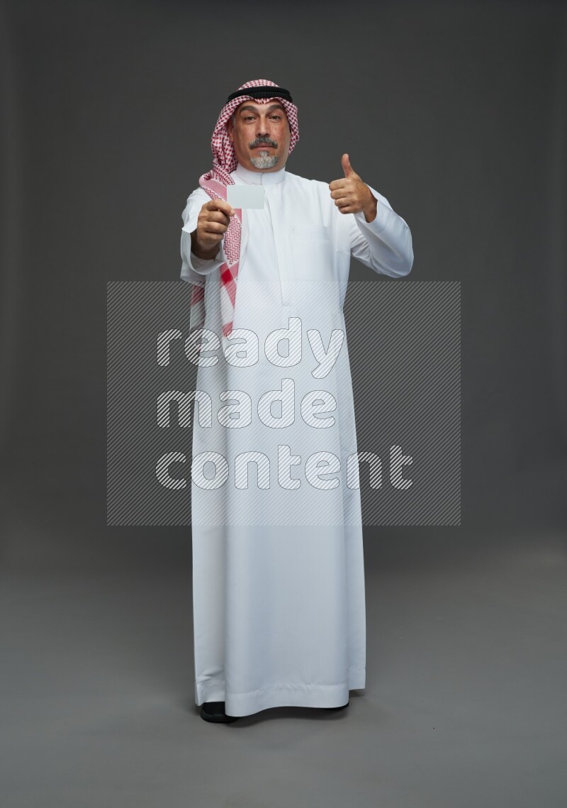 Saudi man with shomag Standing holding ATM card on gray background