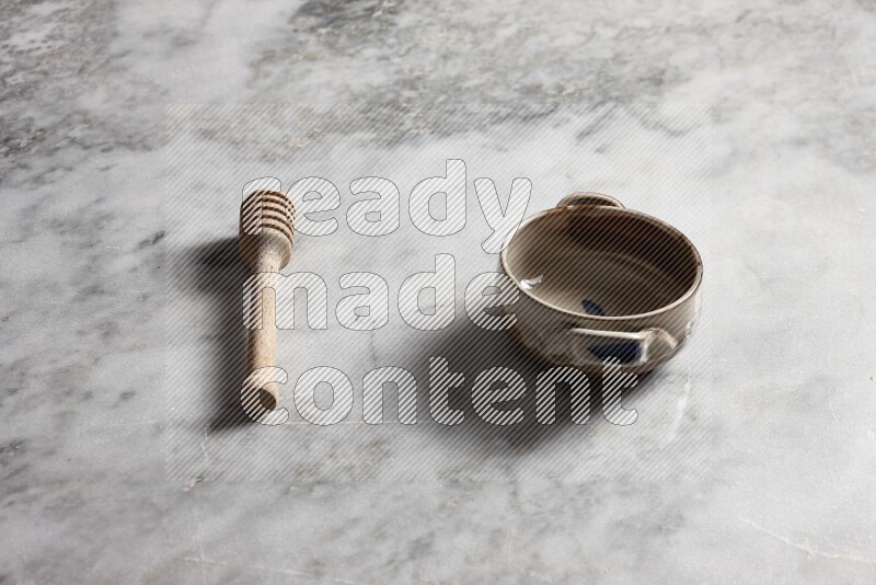 Multicolored pottery bowl with wooden honey dipper on the side on grey marble background