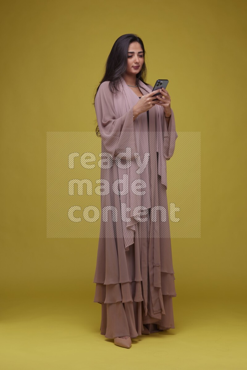 A woman Texting on a Yellow Background wearing Brown Abaya