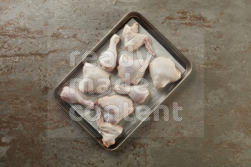 Mixed fresh chicken pieces in an oven tray on a textured rustic background