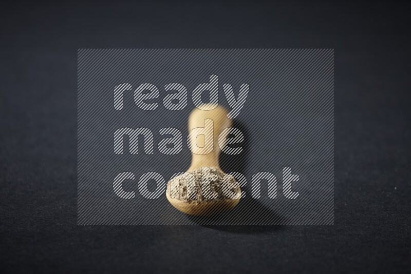 ملعقة خشبية ممتلئة ببودرة الهيل على خلفية سوداء