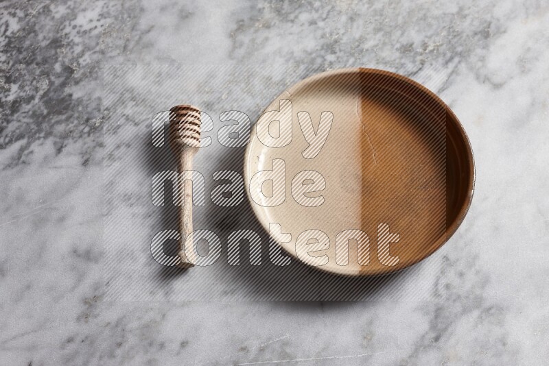 Multicolored pottery oven plate with wooden honey dipper on the side on grey marble background