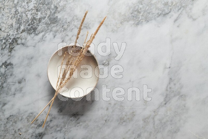 Wheat stalks on beige pottery plate on grey marble background