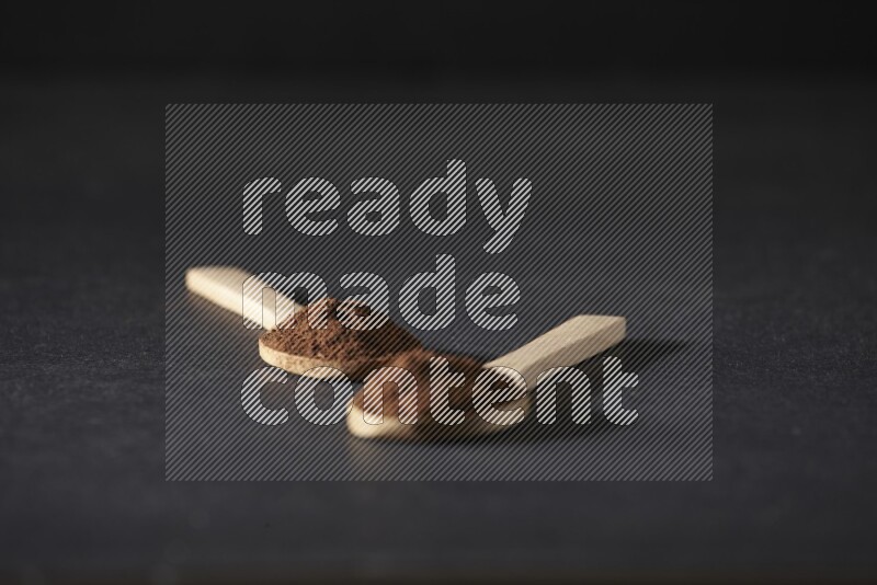 2 wooden spoons full of cloves powder on a black flooring