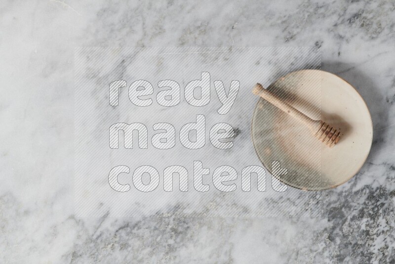 طبق فخاري متعدد الألوان مع ملعقة عسل خشبية بداخله على خلفية من الرخام الرمادي