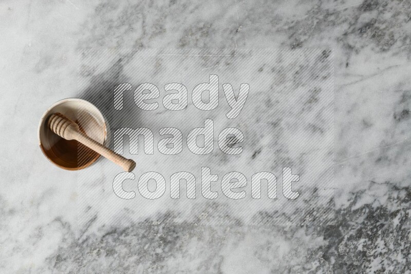 وعاء فخاري متعدد الألوان مع ملعقة عسل خشبية بداخله على خلفية من الرخام الرمادي