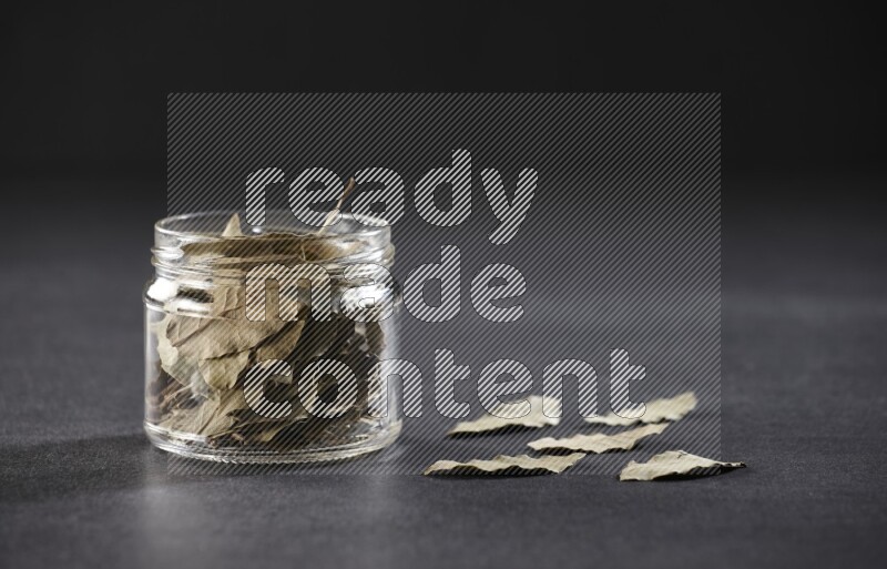A glass jar filled with dried bay leaves on black flooring