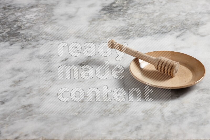Beige pottery plate with wooden honey dipper in it on grey marble background