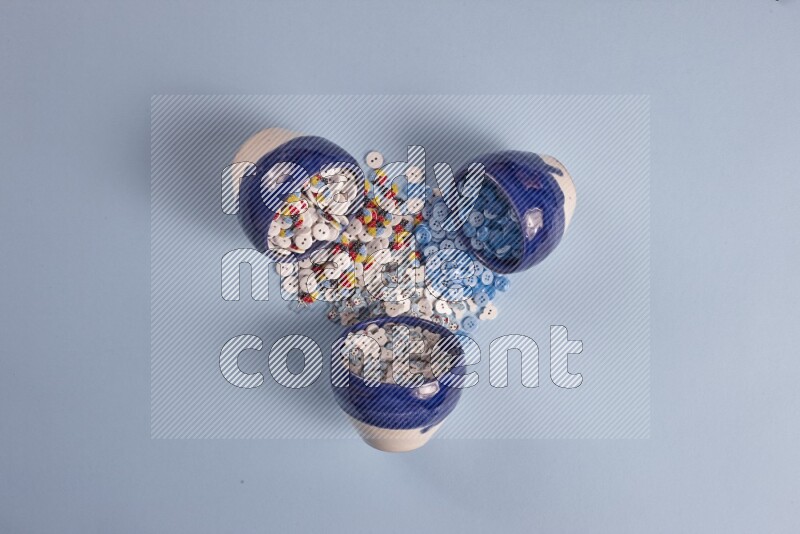 Multicolored pottery bowls full of colored buttons on blue background