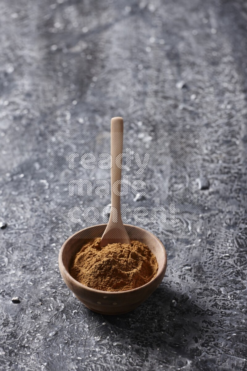 Wooden bowl full of cinnamon powder with a wooden spoon on a textured black background in different angles