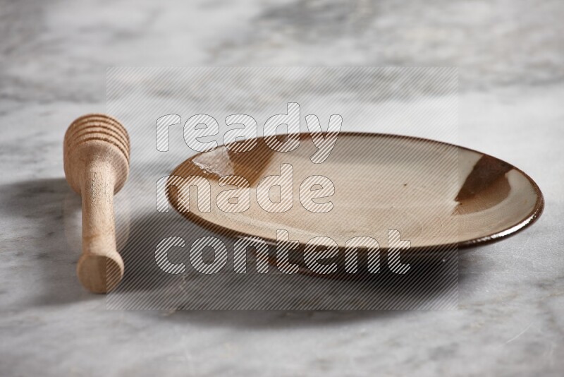 Multicolored pottery plate with wooden honey dipper on the side on grey marble background