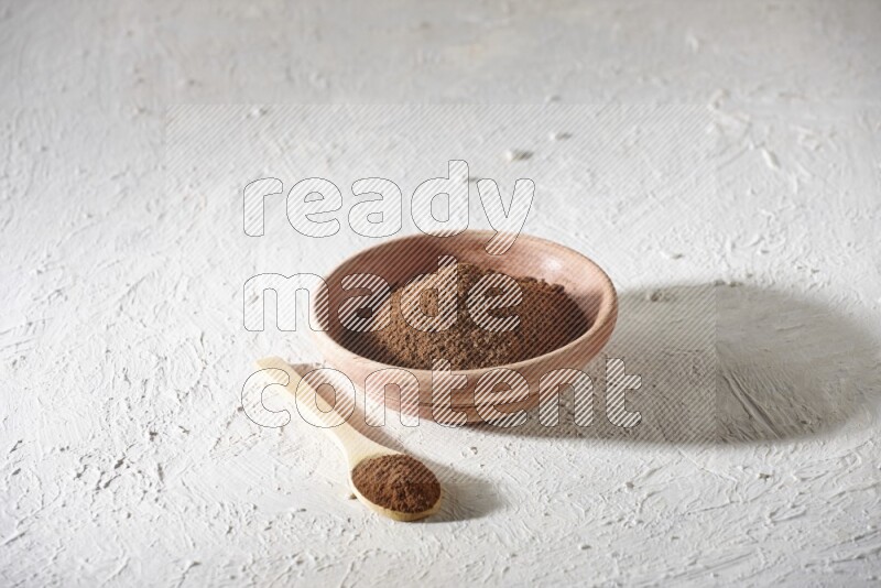 A wooden bowl and a wooden spoon full of cloves powder on a textured white flooring