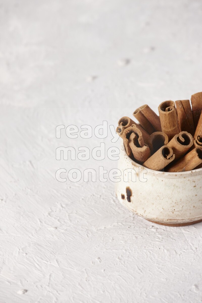 Cinnamon sticks in a beige bowl on a white background