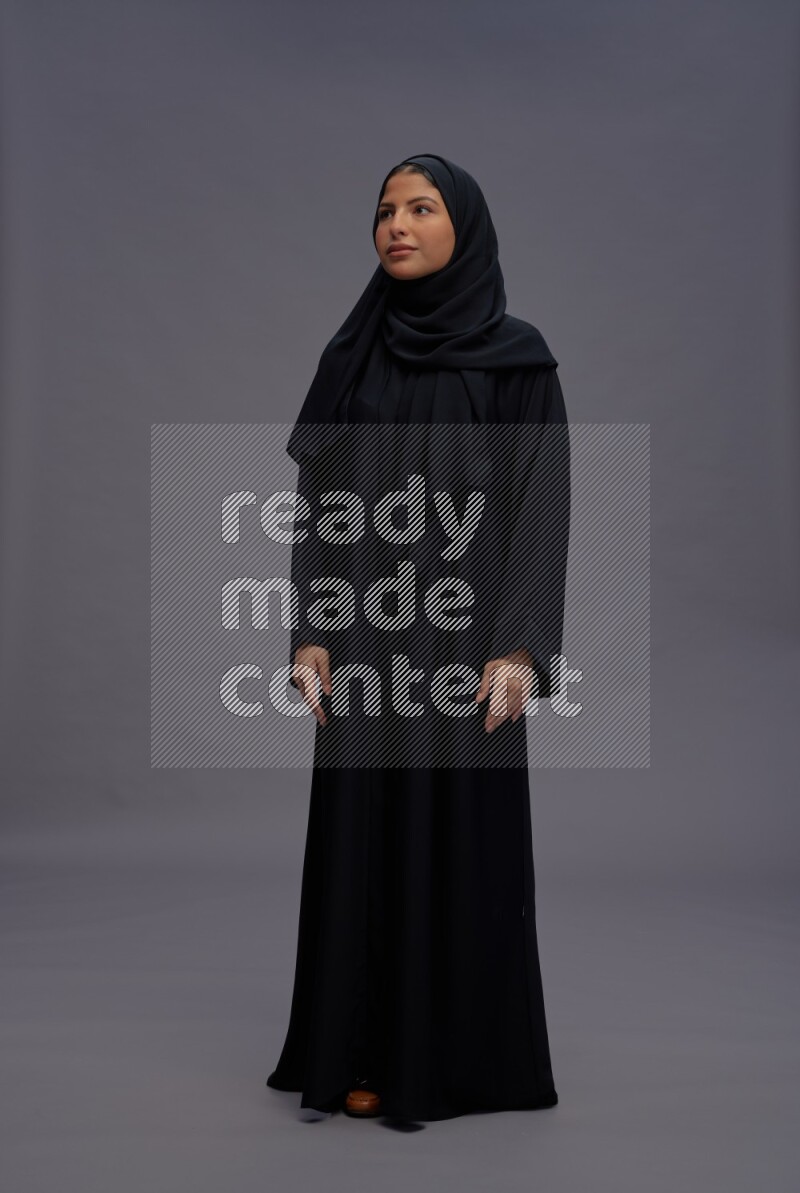 Saudi woman wearing Abaya standing interacting with the camera on gray background
