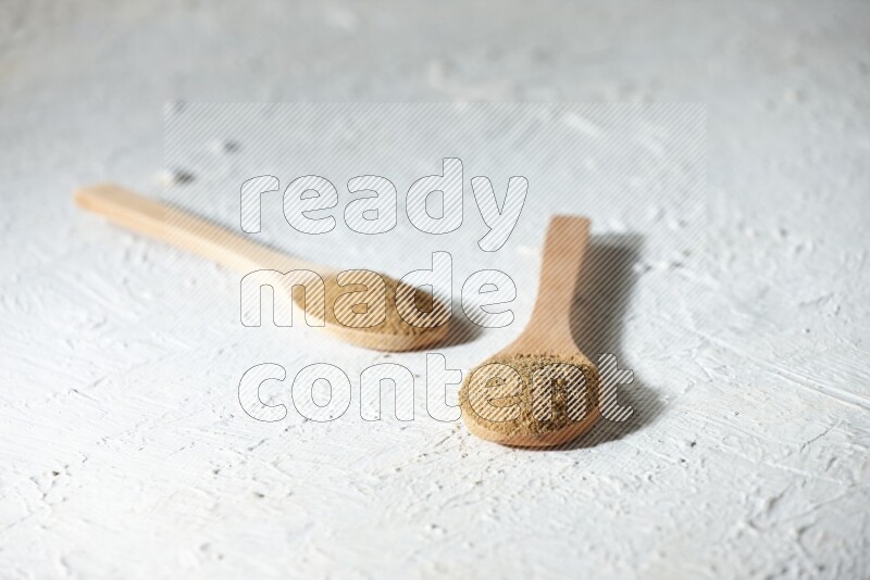 2 Wooden spoons full of cumin powder on a textured white flooring